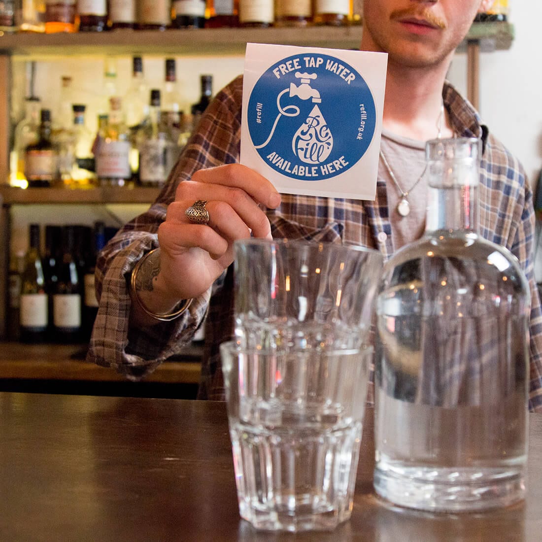SQUARE-sticker-with-water-in-jug-copy man in bar with Refill sticker and two glasses with a bottle of water