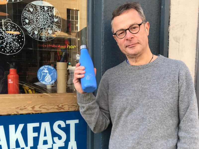 Hugh Fearnley-Whittingstall with a Chilly's Refill bottle next to window sticker outside cafe