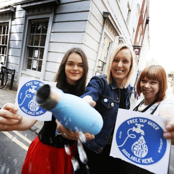 women in street smiling people, holding refill window stickers and bottle