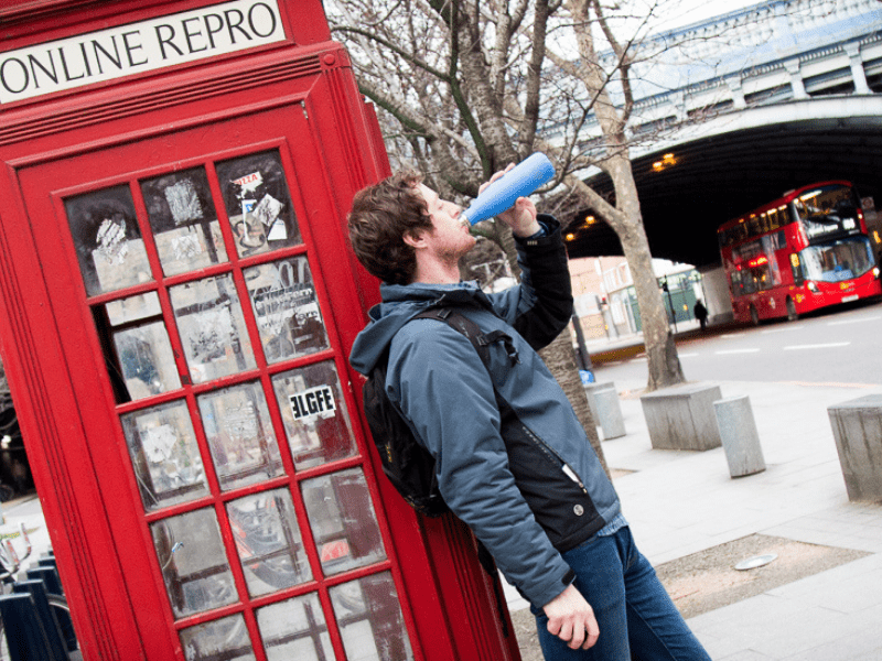 Man drinking from a Refill bottle infront of a red telephone box in London